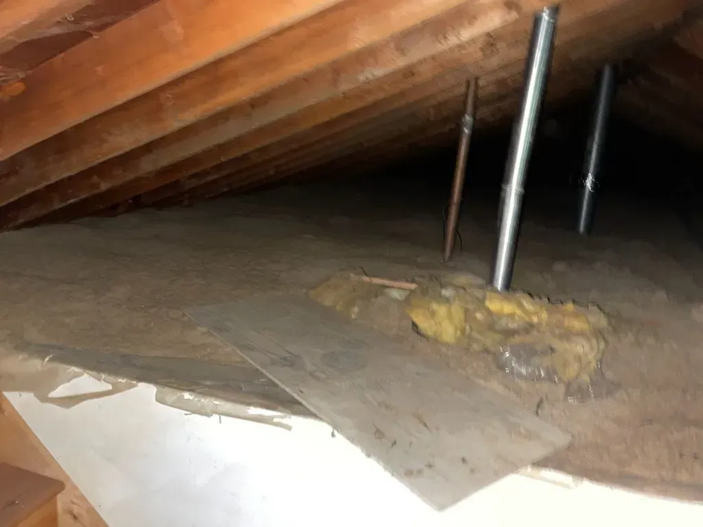 A dirty attic with a lot of wooden beams and a metal pipe hanging from the ceiling.