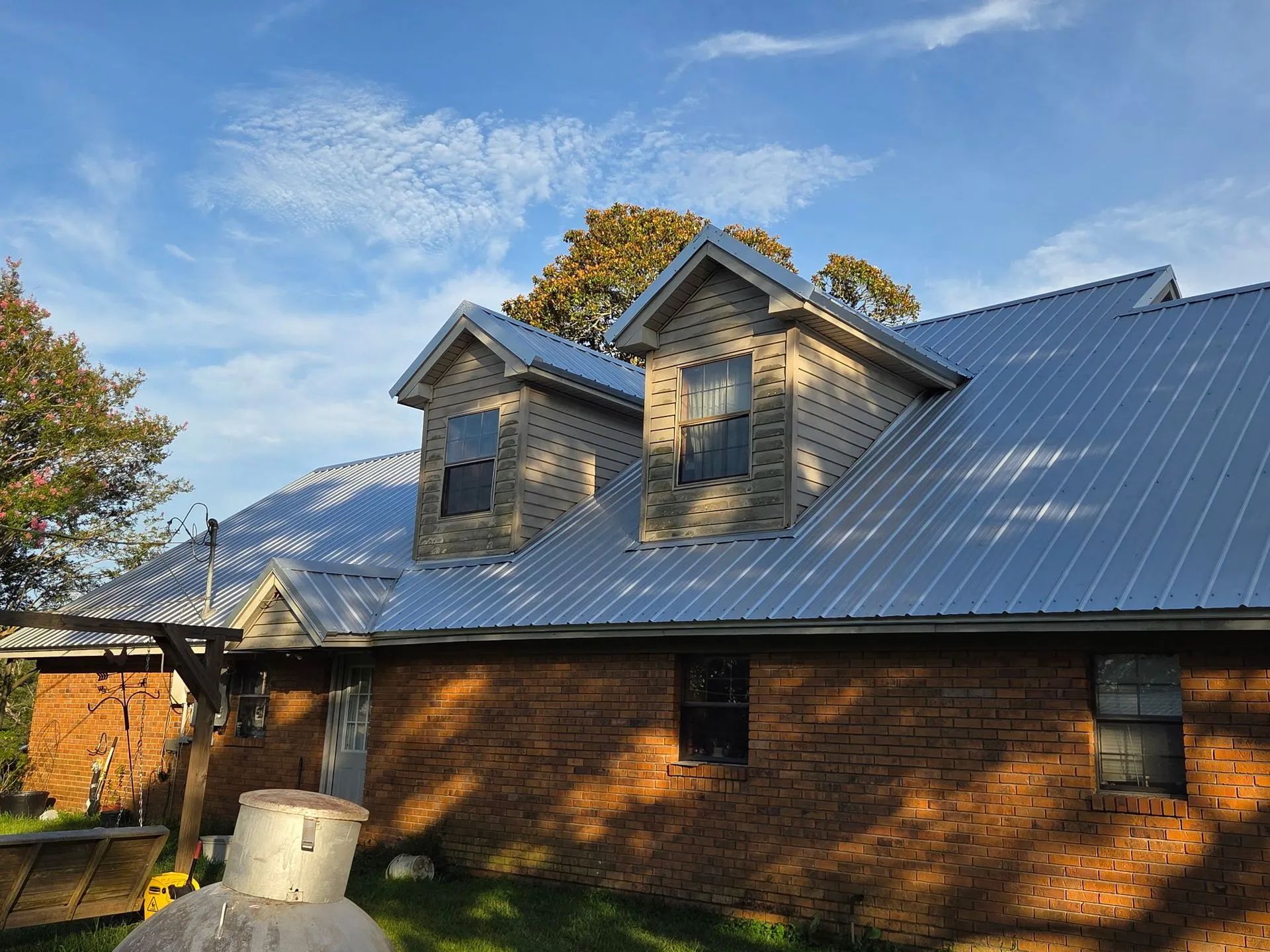 Brick house with metal roof and dormer windows under a blue sky at sunset