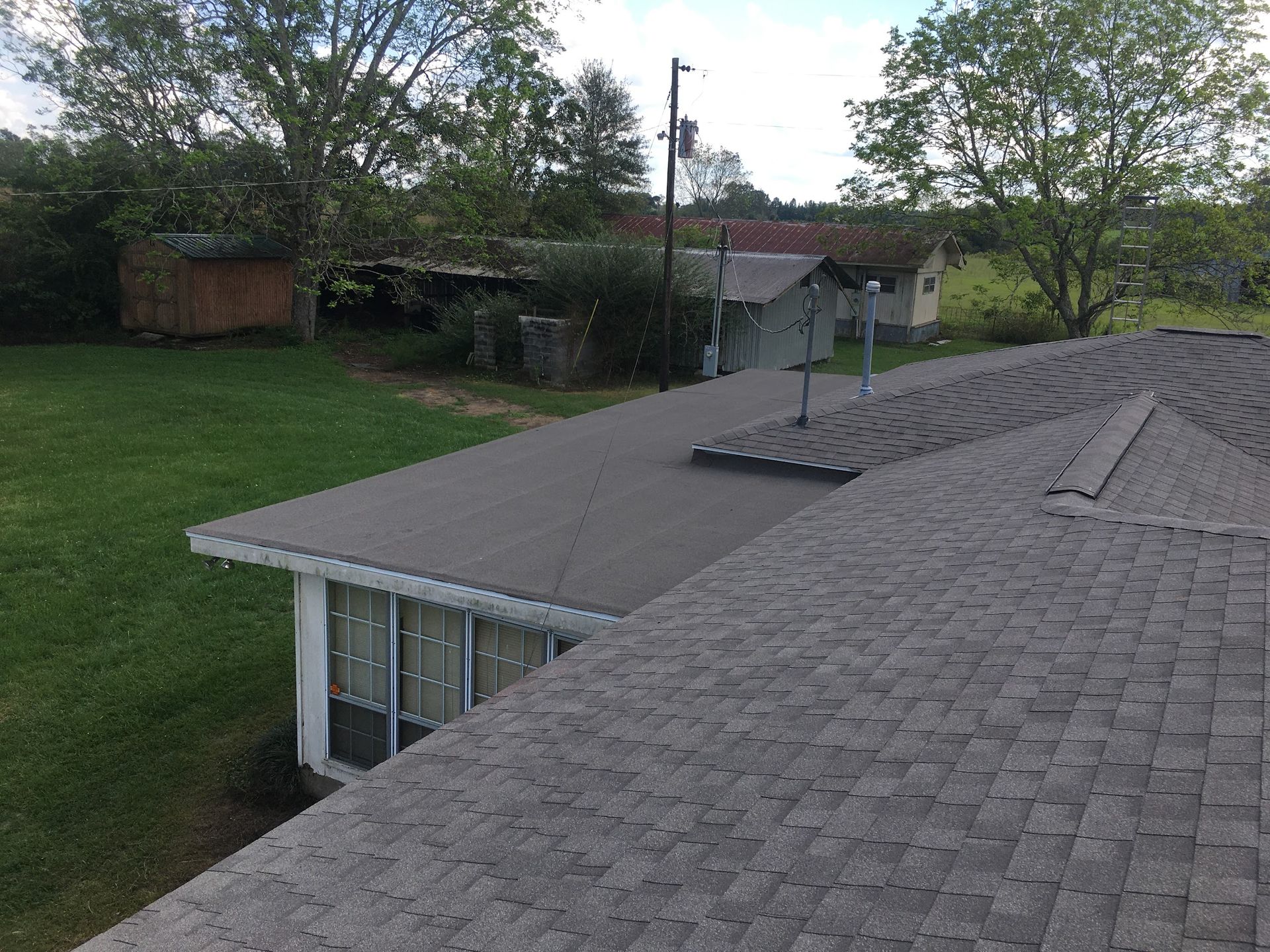 Rooftops with gray shingles overlooking a grassy yard and trees in a suburban neighborhood
