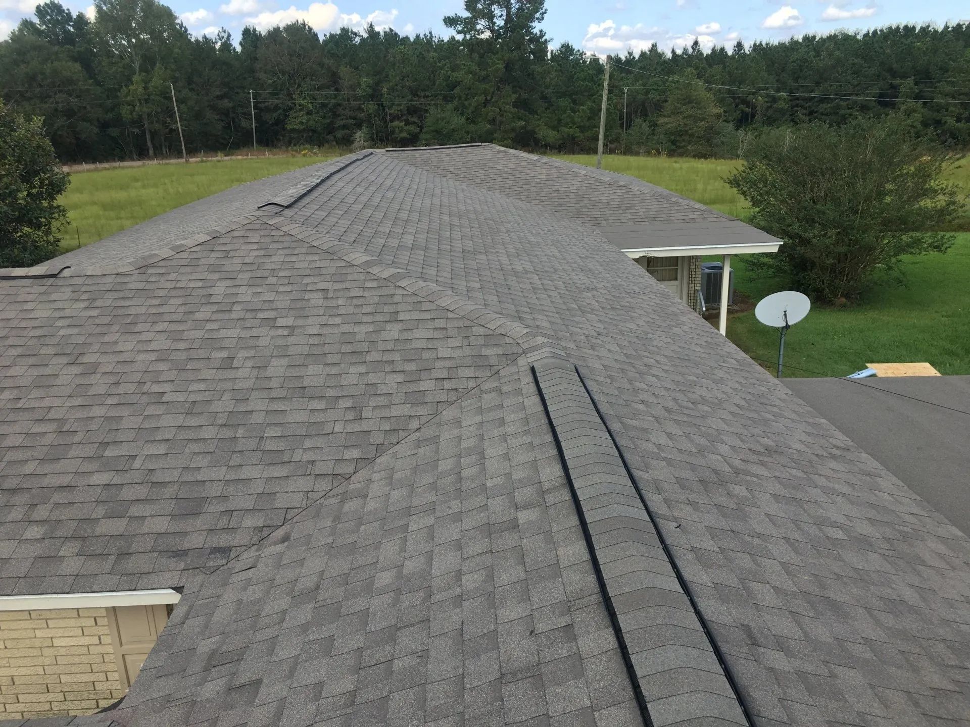 Gray shingle roof of a house with trees and grass in the background.