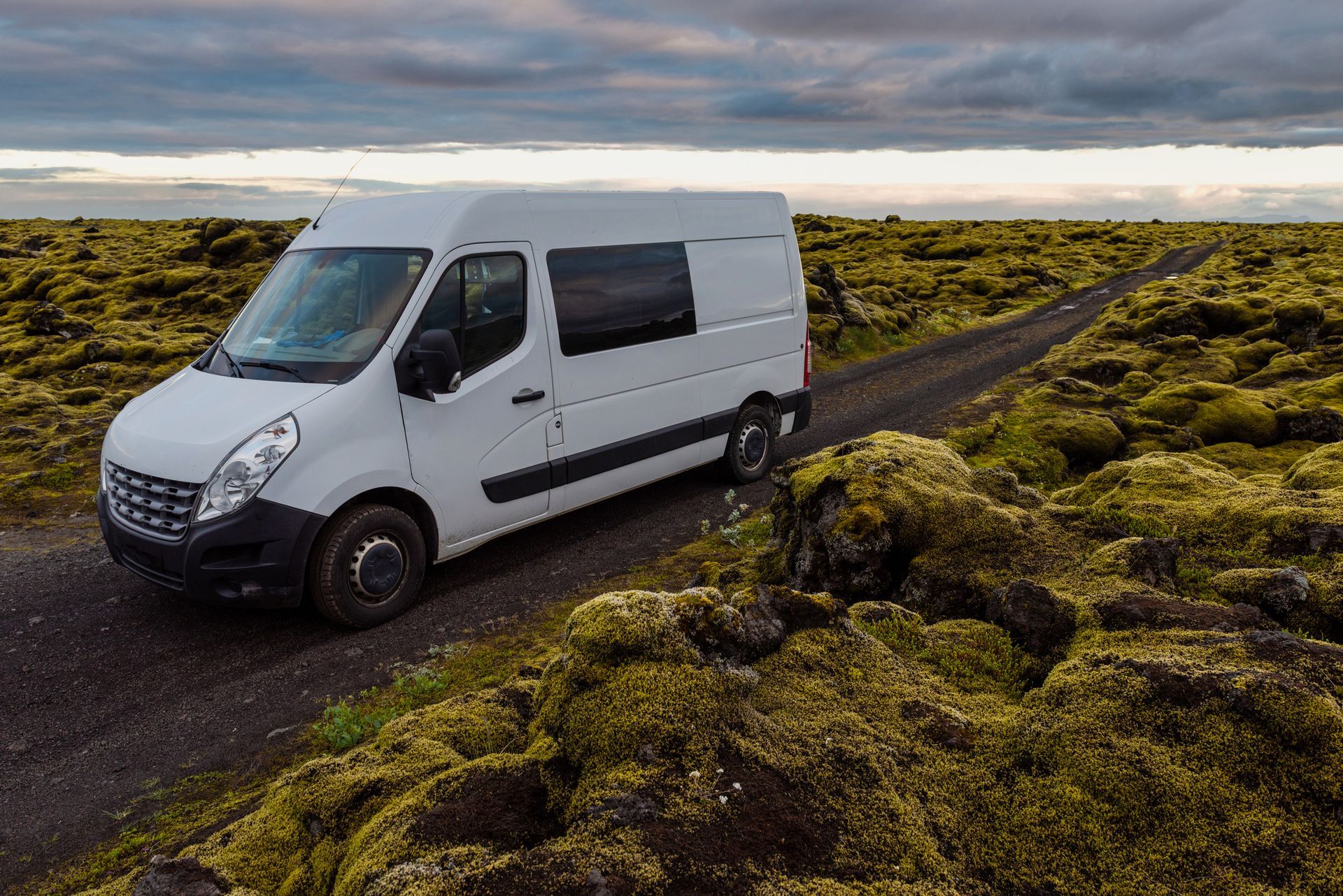 A white van is parked on the side of a dirt road.