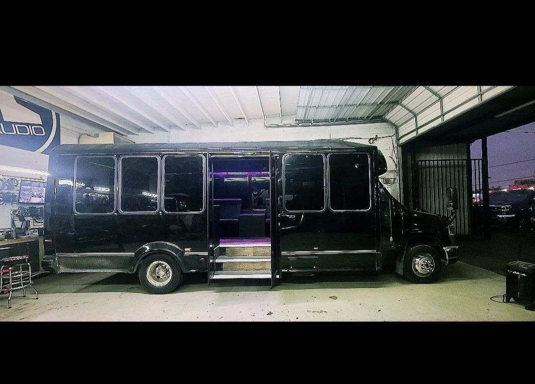 A black bus is parked in a garage with its doors open.