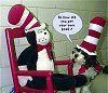 Cat in the Hat plush doll in rocking chair speaking to another doll, both wearing hats.