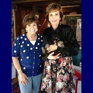 Two women smiling, one holding a small, dark animal; indoors with wooden accents.