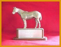 Silver horse trophy on a wooden base with engraved text, set against a red backdrop.