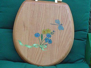 Wooden toilet seat with painted blue flowers, yellow centers, green ribbon, and blue dragonfly.
