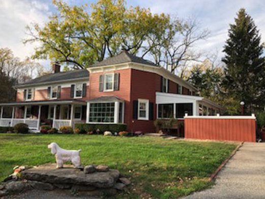 Red brick house with white trim, a porch, and a dog statue on the lawn.