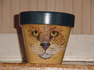 Hand-painted terracotta pot with a leopard face, dark green rim, on a wooden surface.