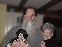 Man with long white beard and woman holding a black and white puppy.