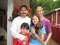 Family of four with a small brown dog pose on a porch.