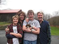 Family of four and a puppy posing in front of a barn.