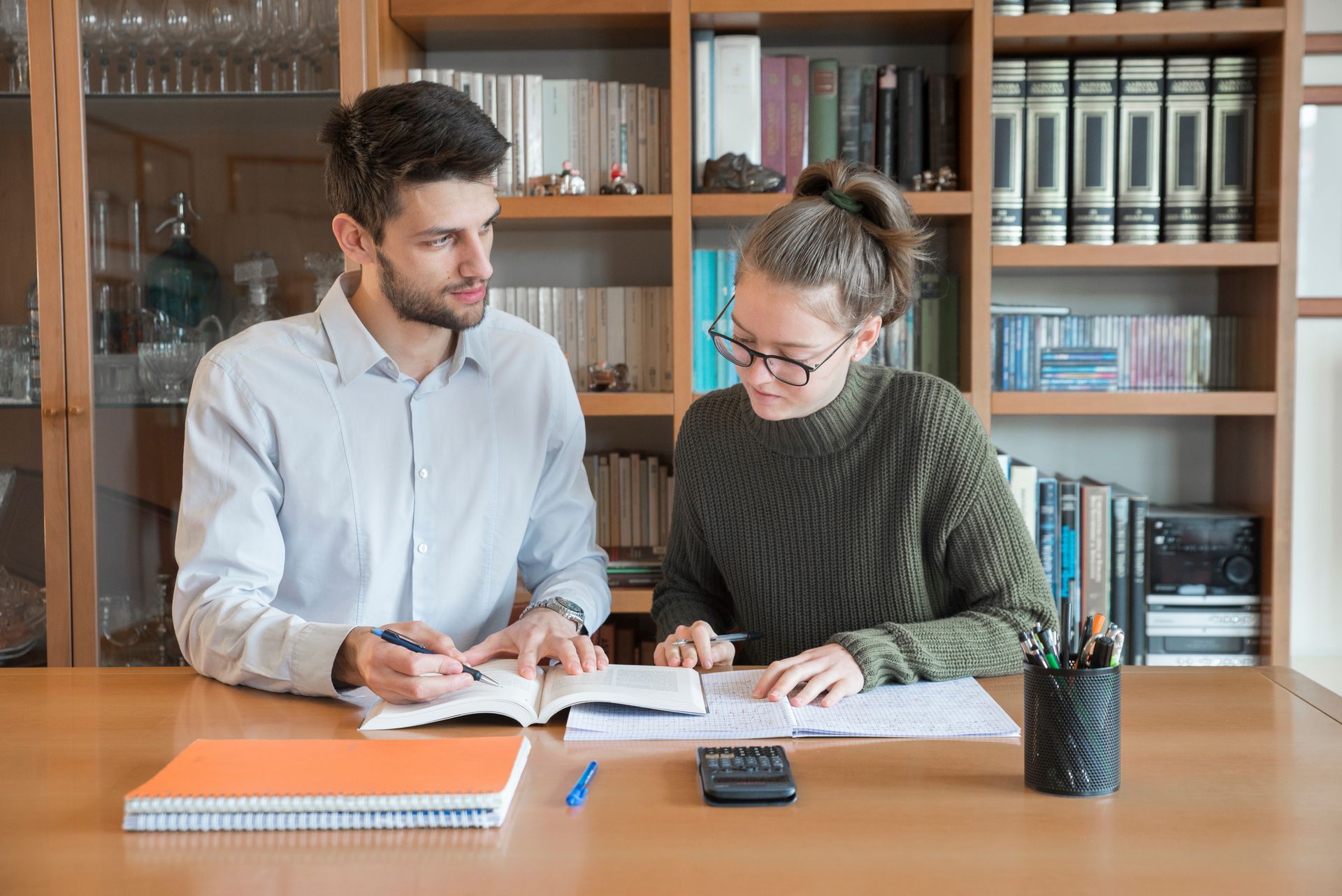 A man and a woman are sitting at a table looking at a book.
