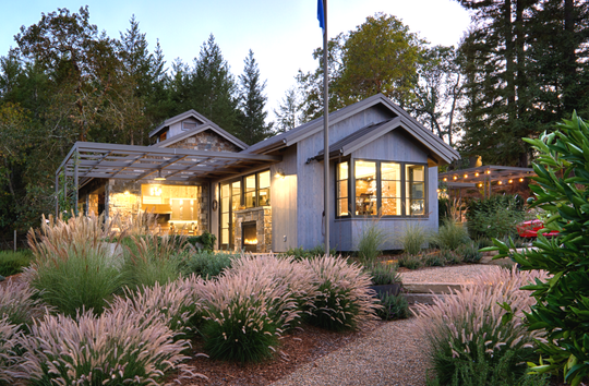 Small gray building with glass windows, flag, surrounded by landscaping, trees.