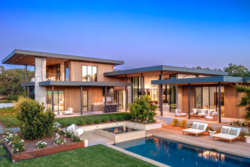 Modern luxury home with pool, landscaping, and outdoor seating. Evening view with blue sky and warm lighting.
