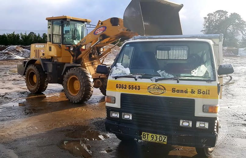 A yellow bulldozer is loading sand into a truck — Pigot's Mid Western Sand and Soil In Orange, NSW