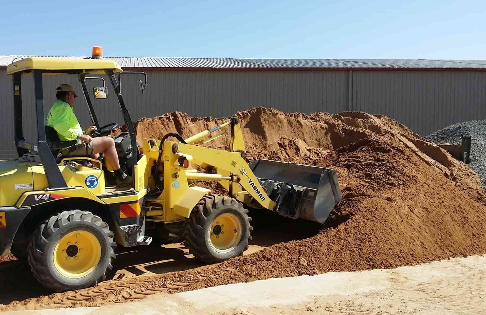 A man is driving a yellow tractor next to a pile of dirt — Pigot's Mid Western Sand and Soil In Orange, NSW