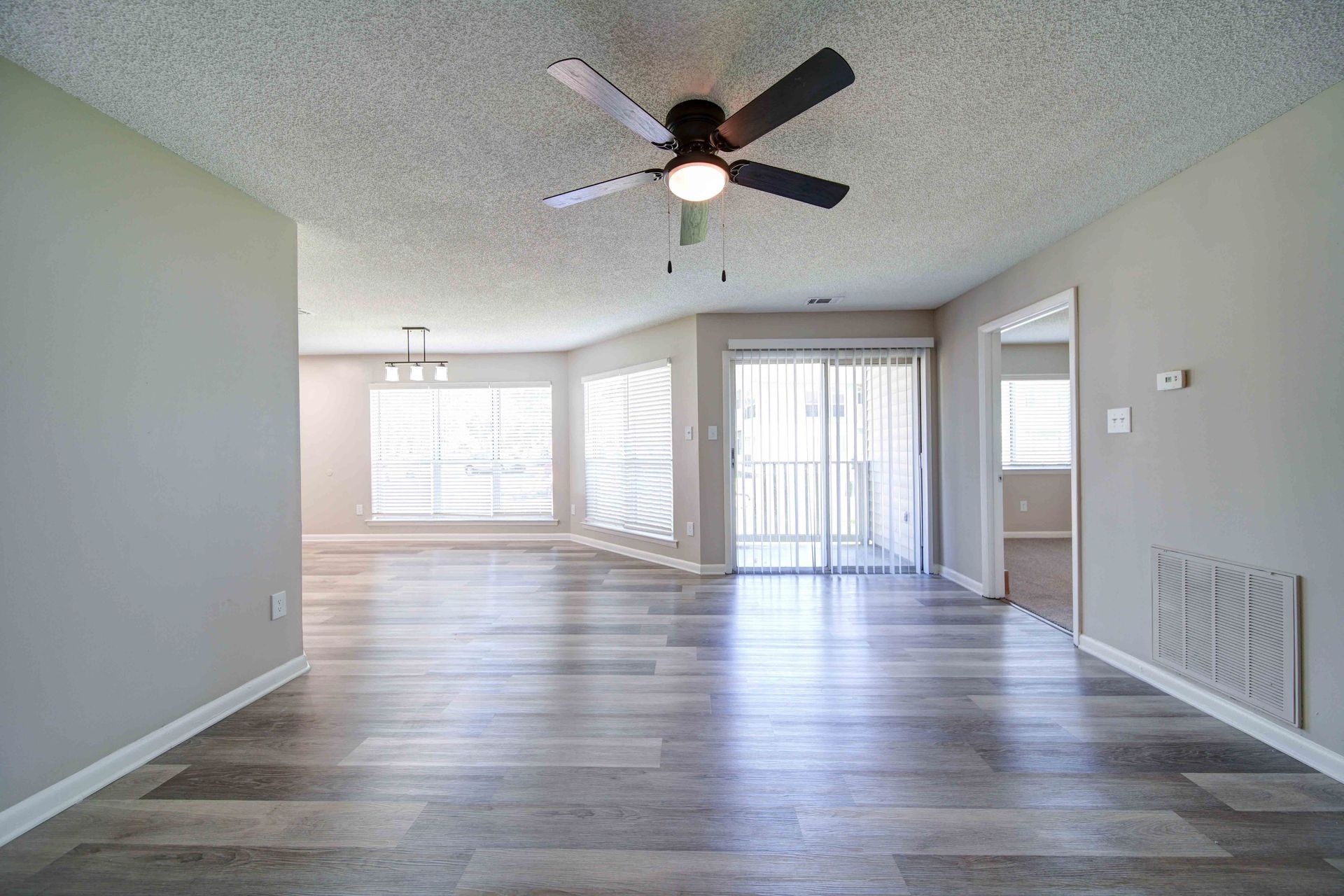 An empty living room with a ceiling fan and sliding glass doors.