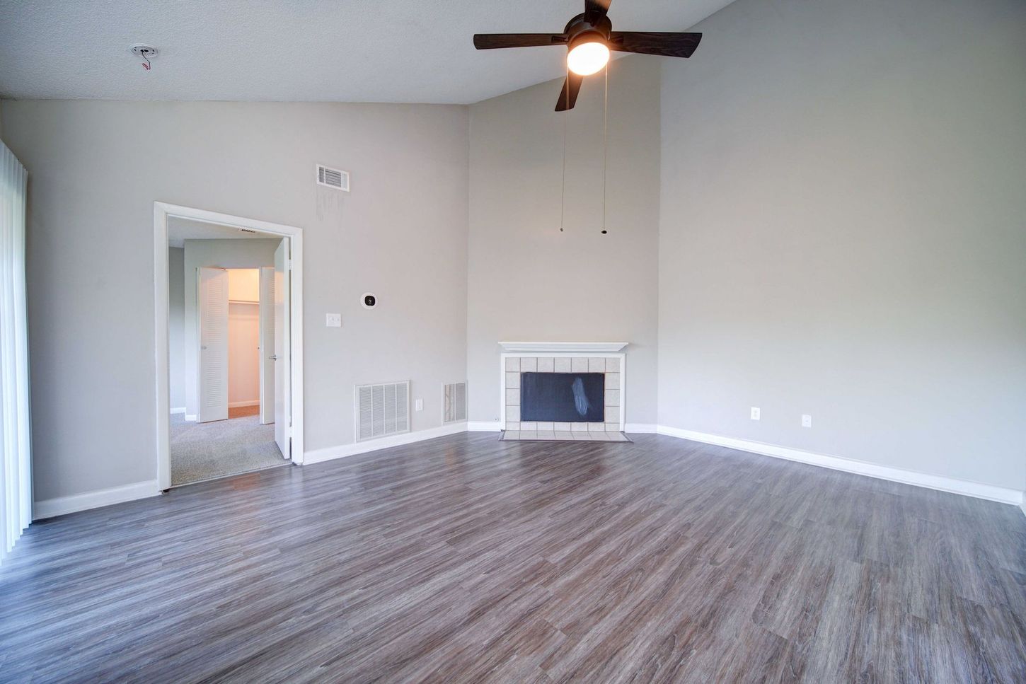 An empty living room with a fireplace and ceiling fan.