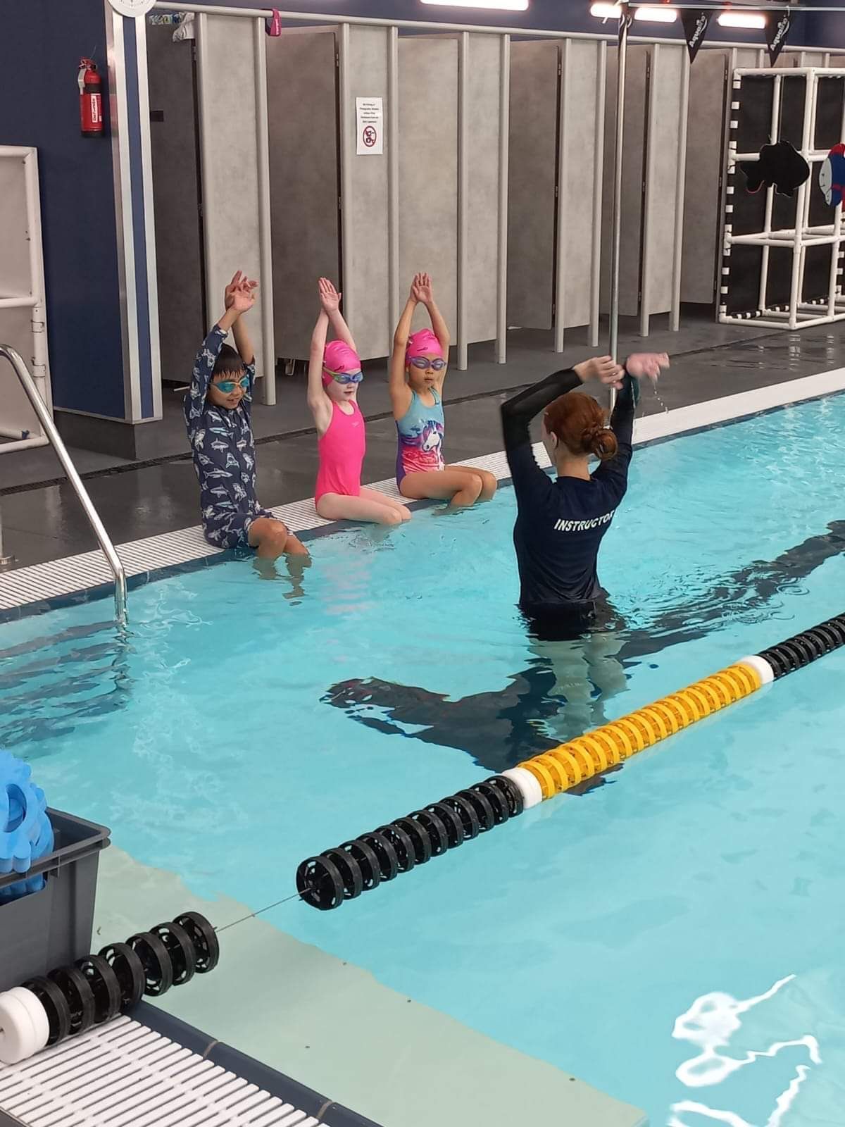 A group of children are sitting on the edge of a swimming pool.