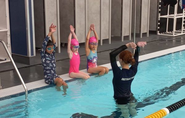 A group of young girls are sitting on the edge of a swimming pool.