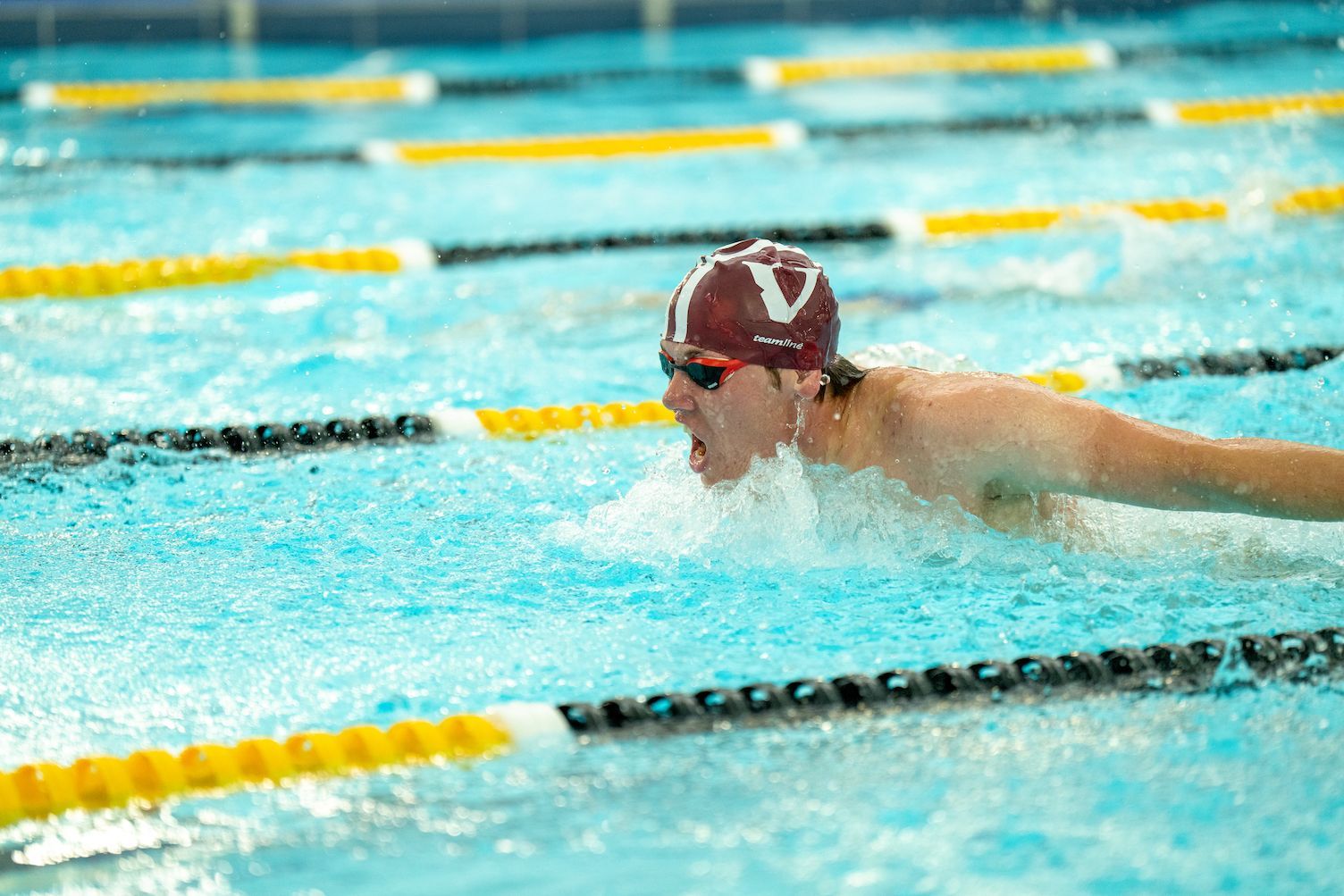 A man is swimming in a swimming pool wearing a red hat and goggles.
