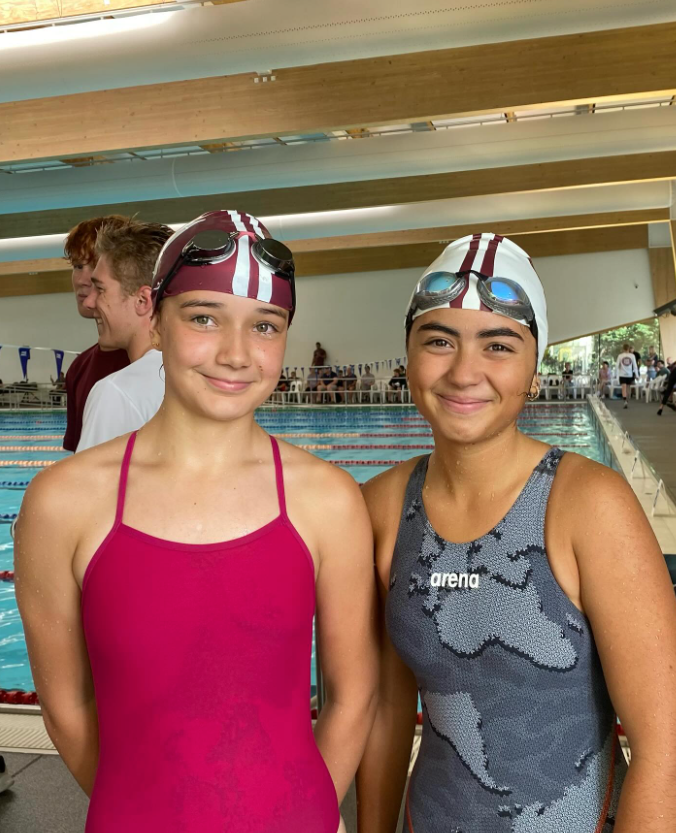 Two young girls are standing next to each other in front of a swimming pool.