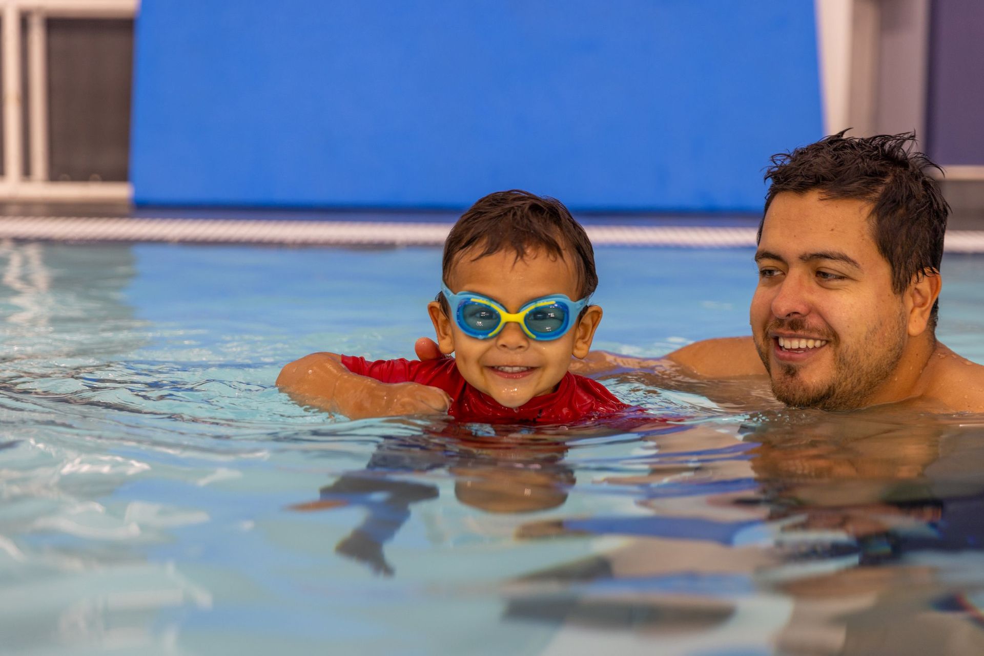 A man is teaching a young boy how to swim in a swimming pool.