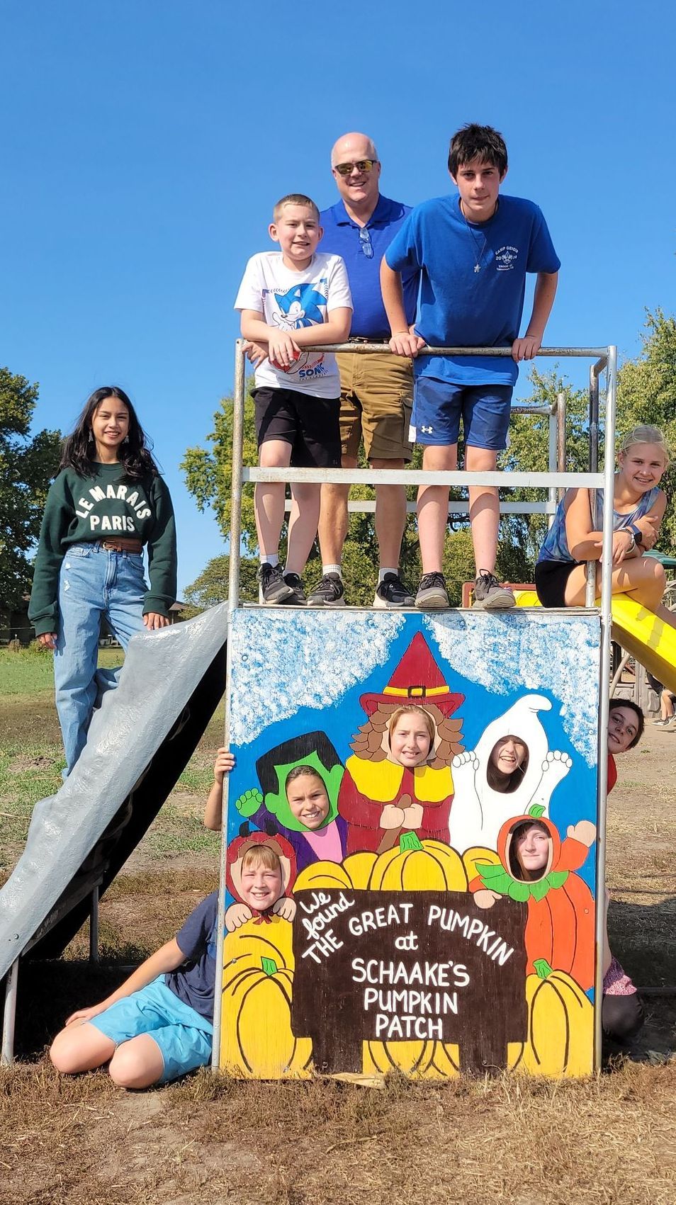 A group of children are standing on top of a pumpkin patch sign.