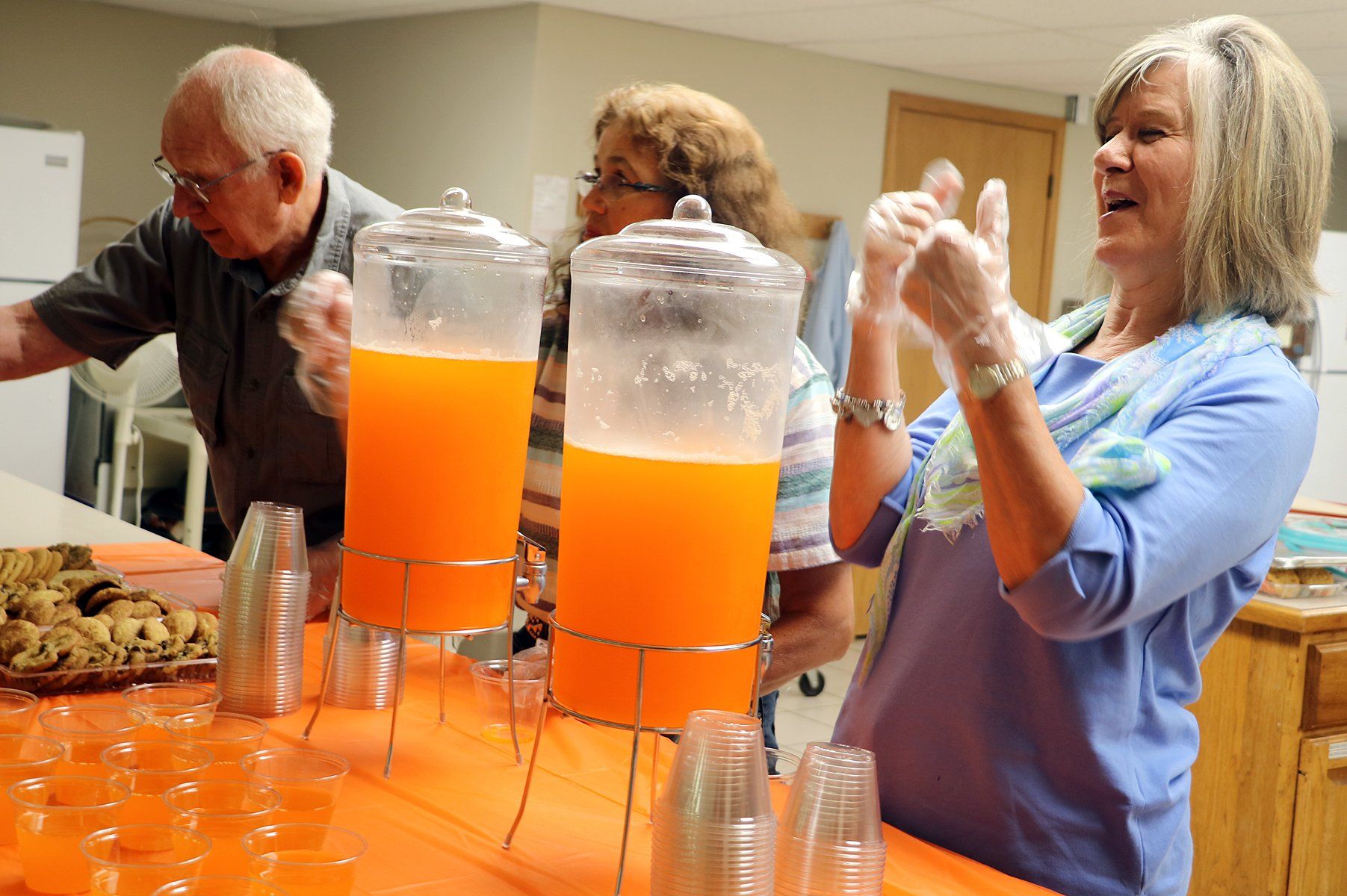 A group of people are pouring orange juice into plastic cups.