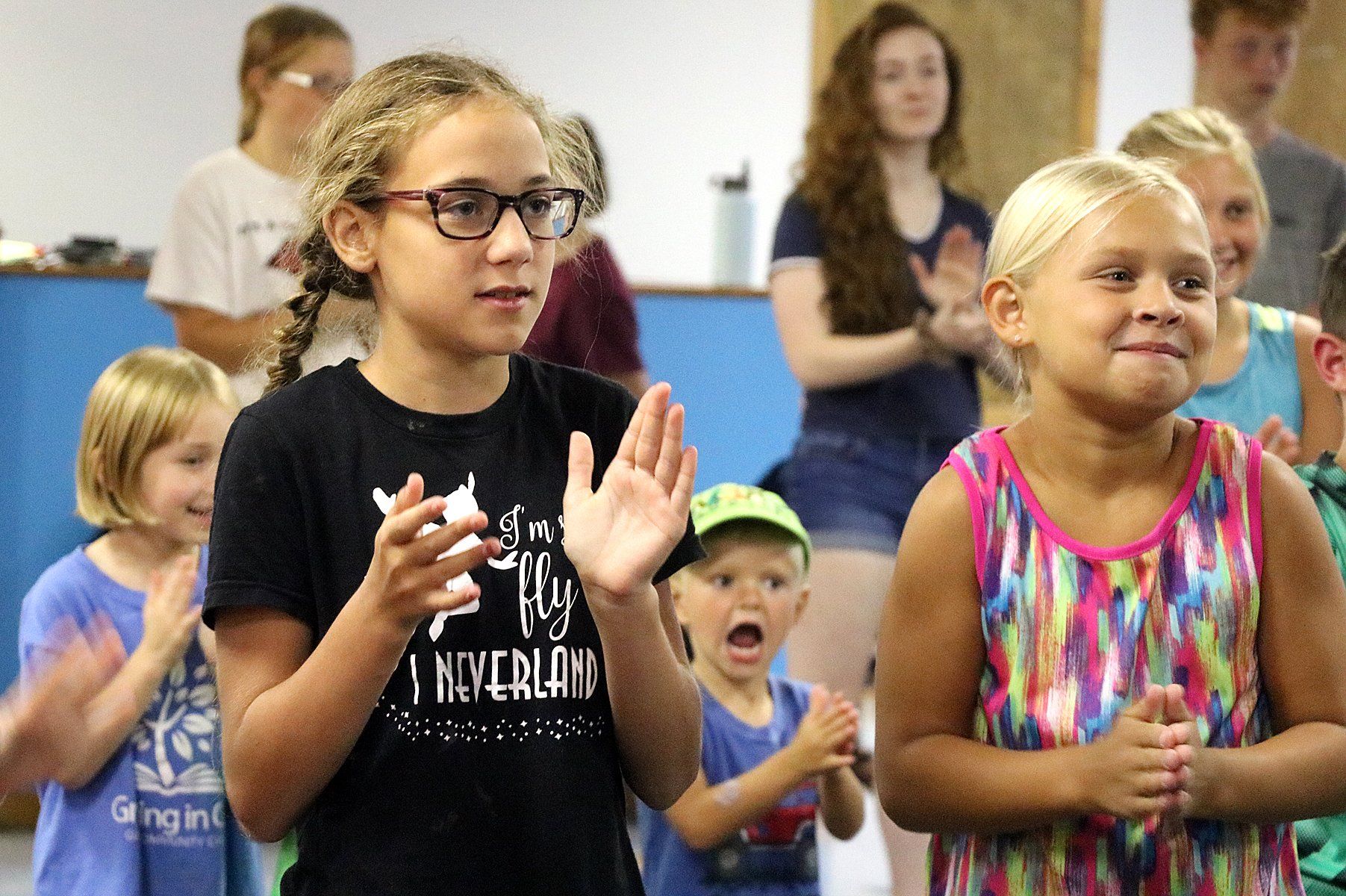 A group of young girls and boys are clapping their hands in a room.