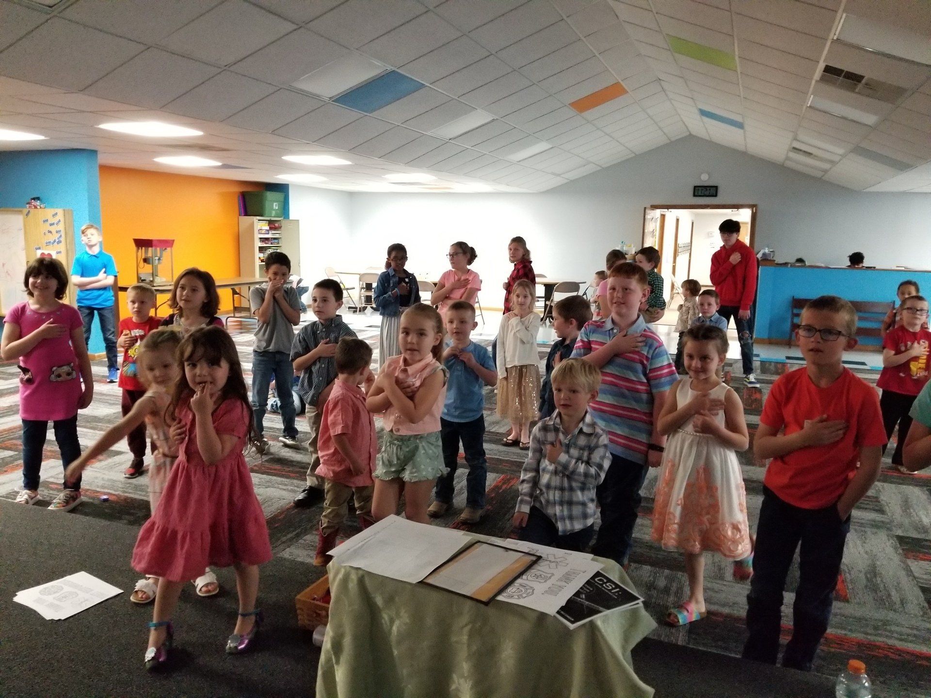 A group of children are standing in a room with their hands on their chests.