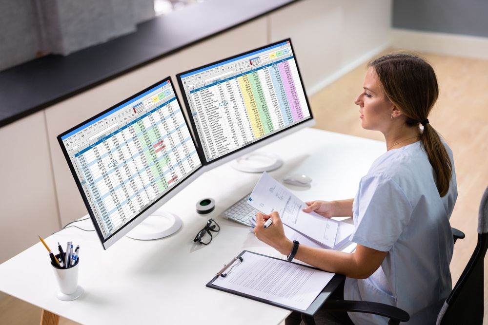 A nurse is sitting at a desk in front of two computer monitors.