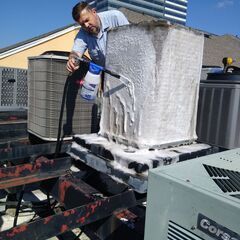 A man is cleaning an air conditioner on the roof of a building.