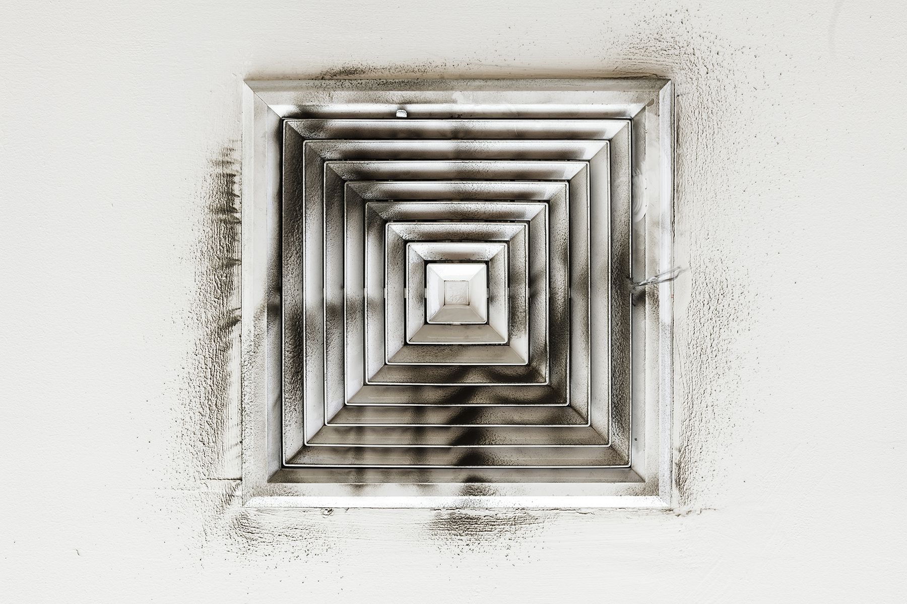 A black and white photo of a dirty air vent on a wall.