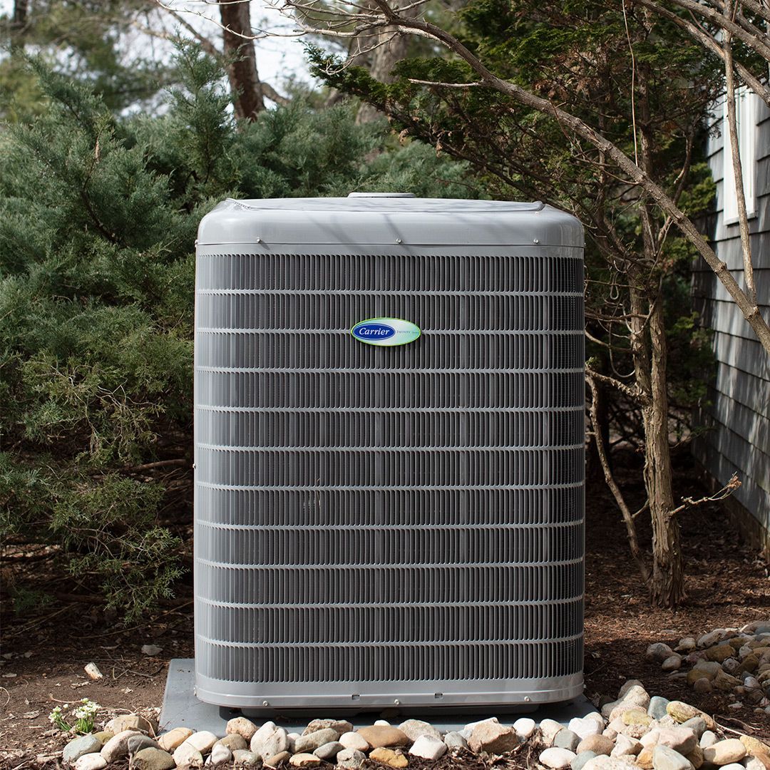 A large gray air conditioner is sitting outside of a house.