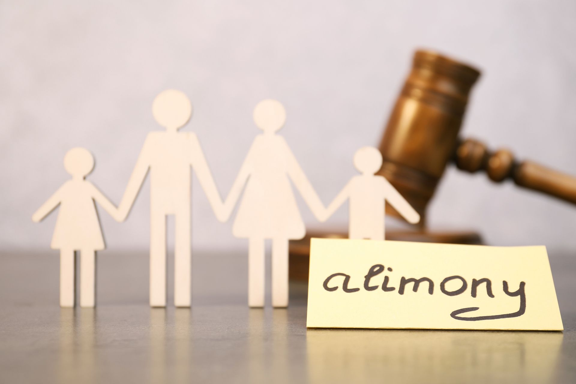 A paper cutout family with a gavel and alimony note at a table, symbolizing legal family matters