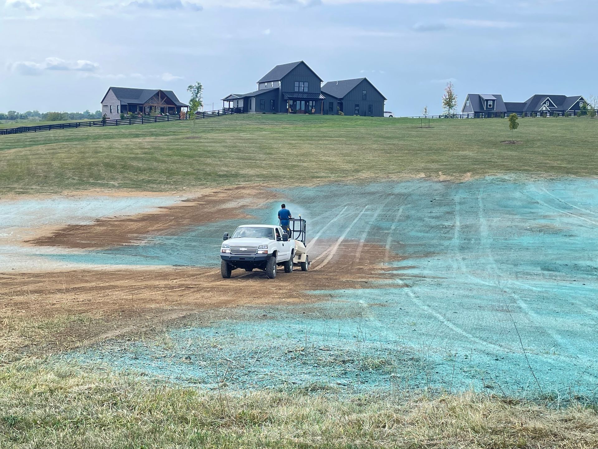Person standing by white car on a dirt road in a wide open field with houses in the distance