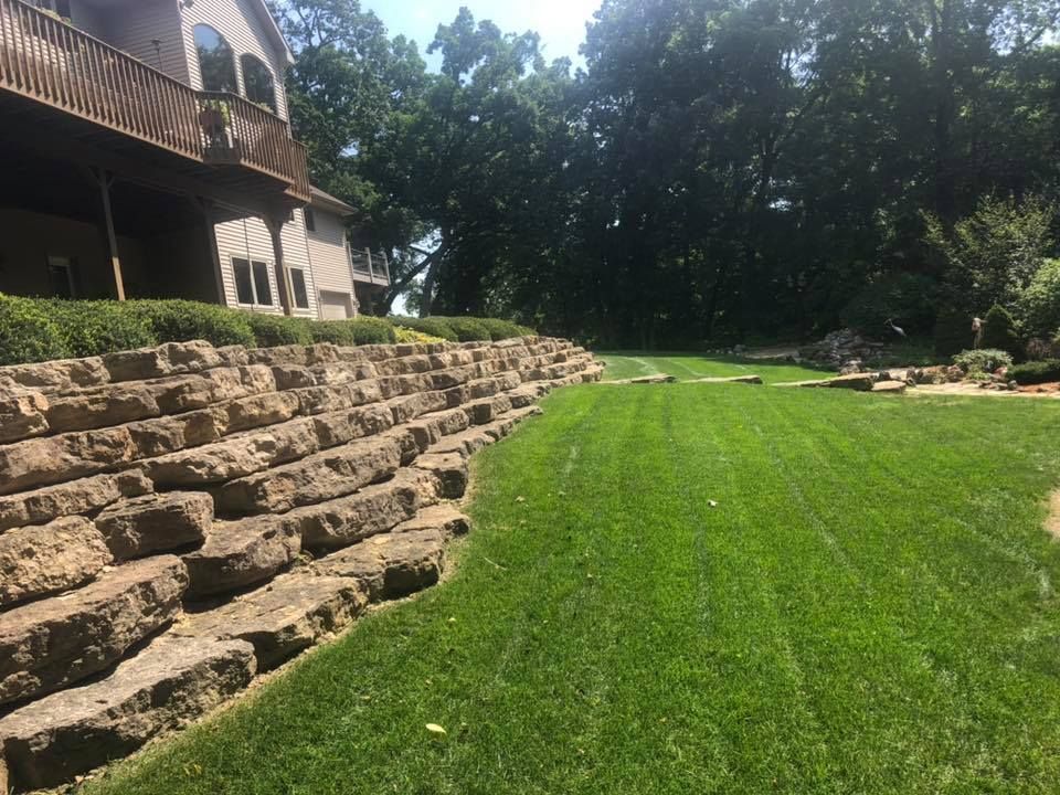 A large lawn with a stone wall in the background and a house in the background.