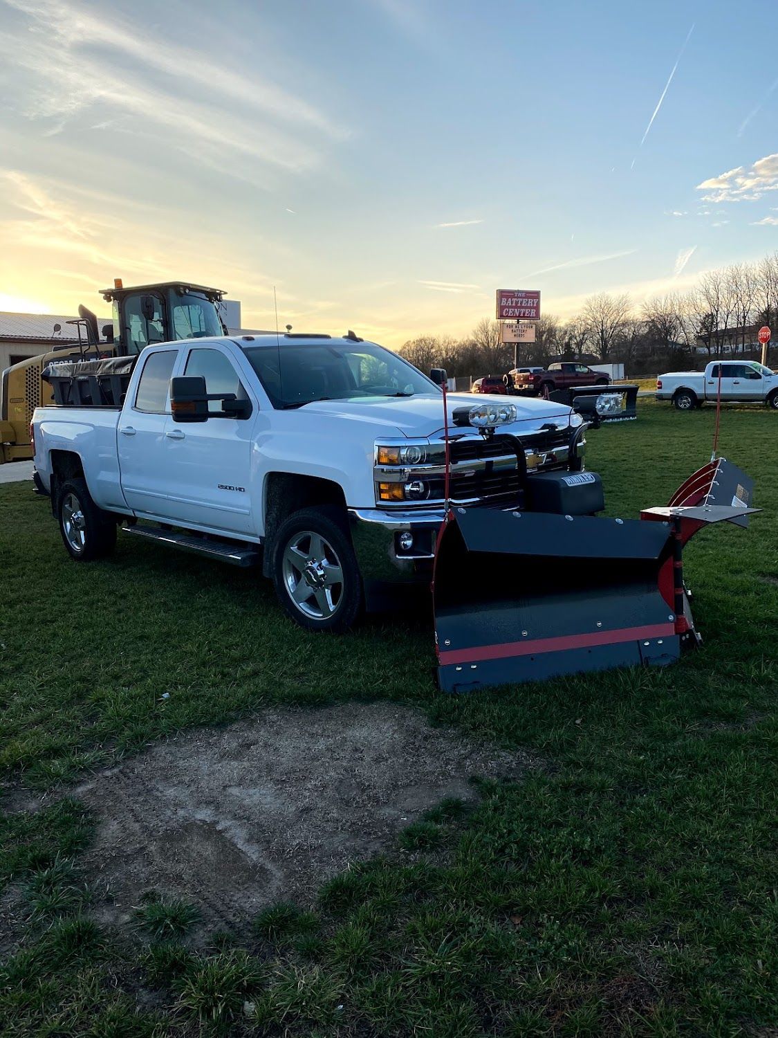 A white truck with a snow plow attached to it is parked in a grassy field.