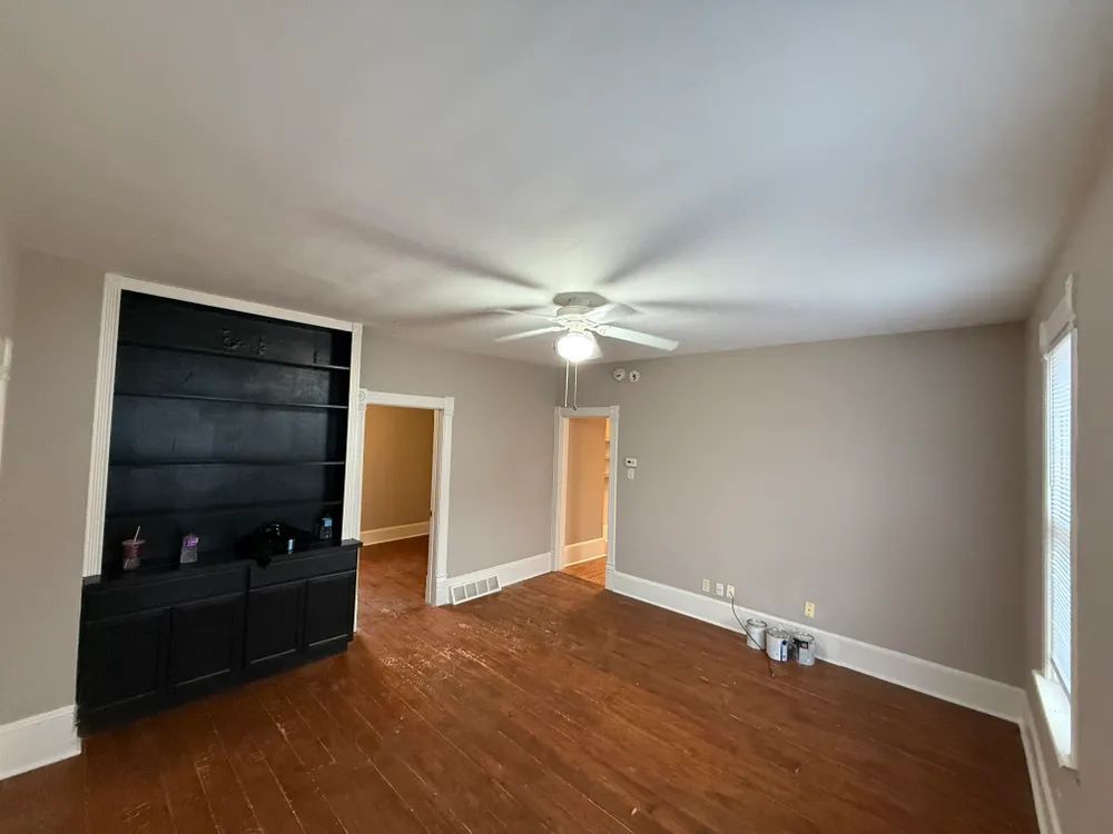 An empty living room with hardwood floors and a ceiling fan.