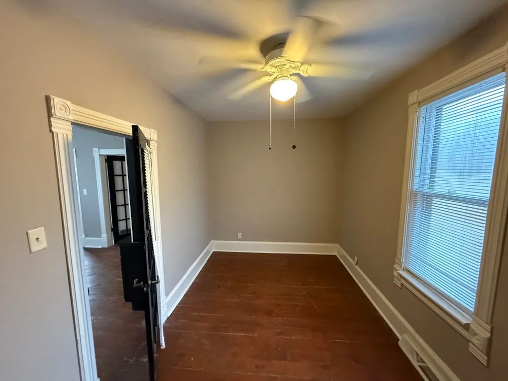 An empty room with a ceiling fan and a window.