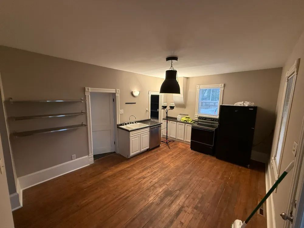 An empty kitchen with hardwood floors and a black refrigerator.