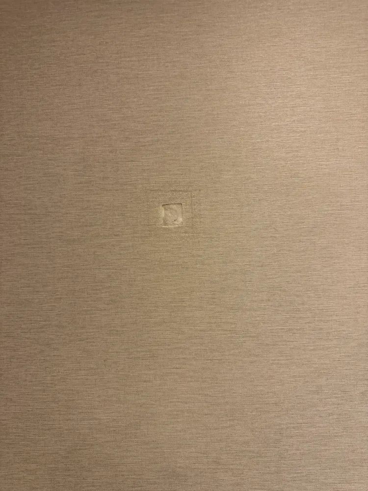 A close up of a beige wall with a hole in it.
