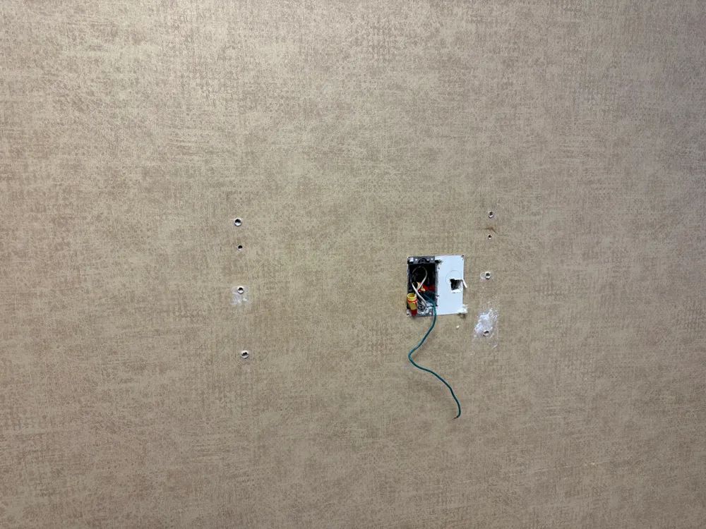 There is a hole in the wall with a wire sticking out of it.