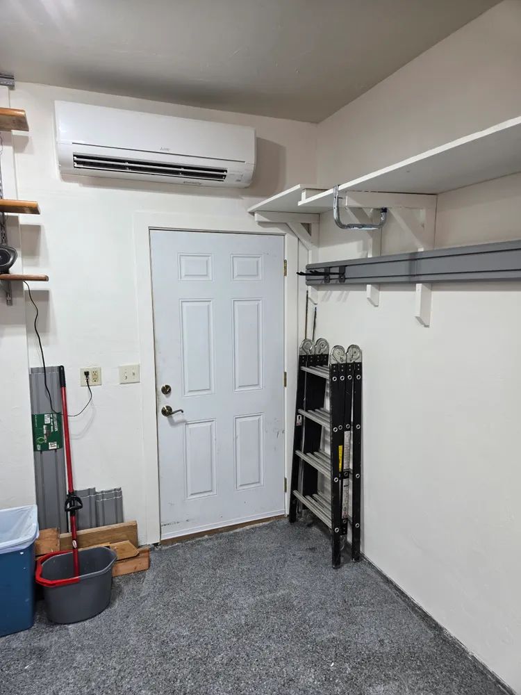 A garage with a door , shelves , a mop and a ladder.