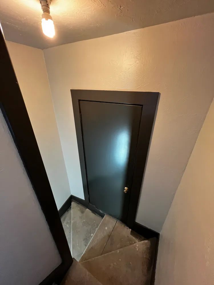 A staircase with a black door and a light on the ceiling.