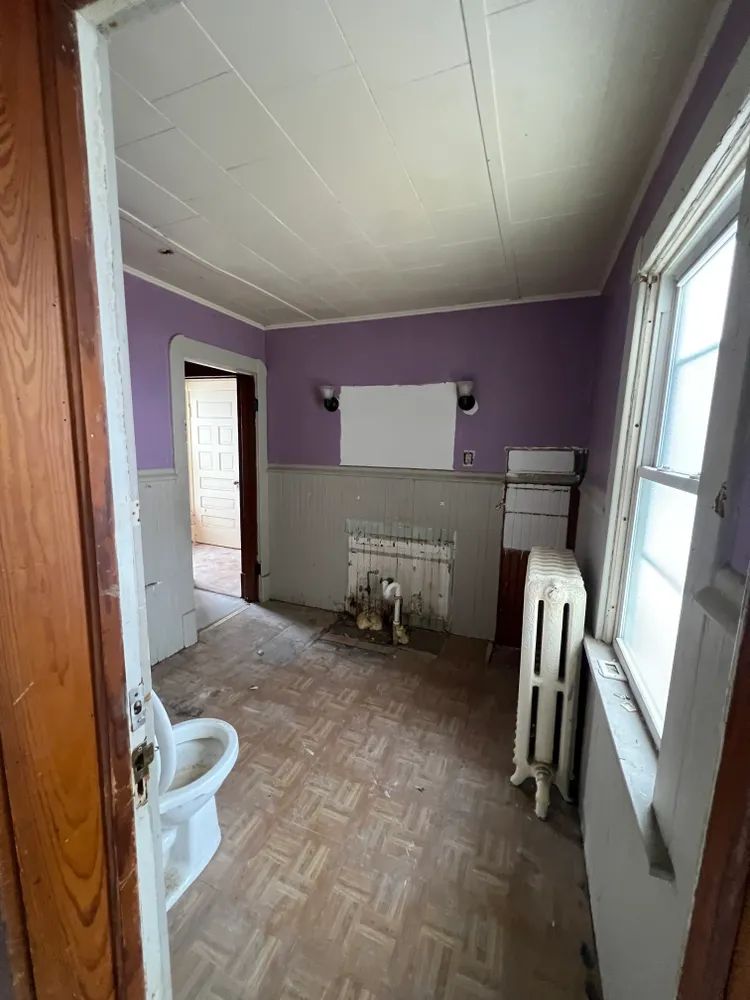 A bathroom with purple walls , a toilet , and a radiator.