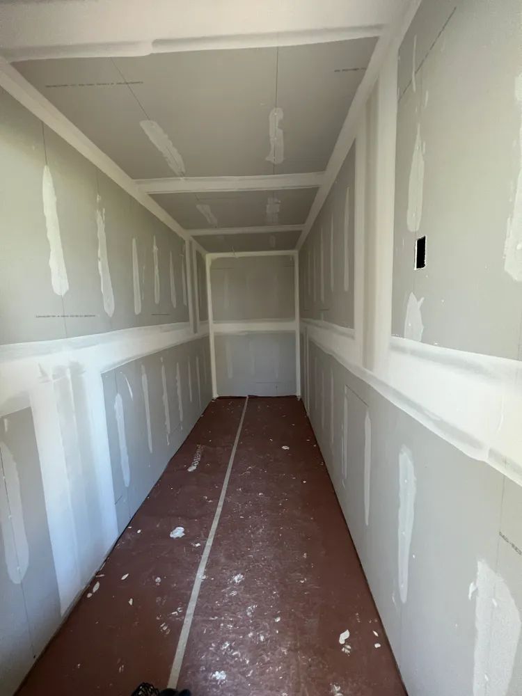 A long hallway with drywall walls and a red floor.