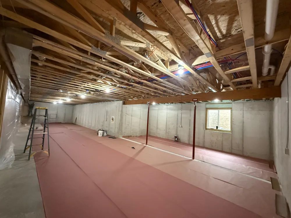 A large empty basement with a red carpet and wooden beams.