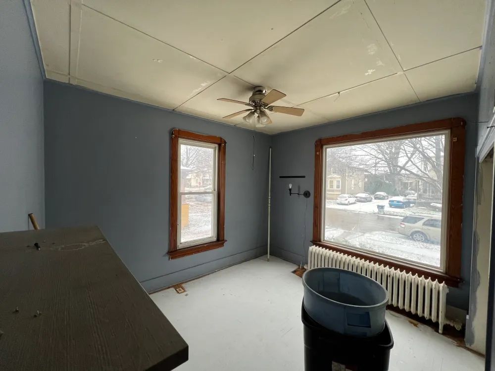 An empty room with a ceiling fan and two windows.